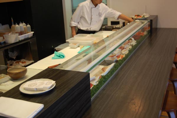 <b>YOKO</b> (Compagnie Française de l'Orient et de la Chine) - 170, bd Haussmann - Paris VIIIe<br/><br/>Vitrine à sushi sur mesure sur châssis inox et habillage en marbre Blackwood.<br/>La grosse tubulure de froid permet la bonne conservation des aliments.