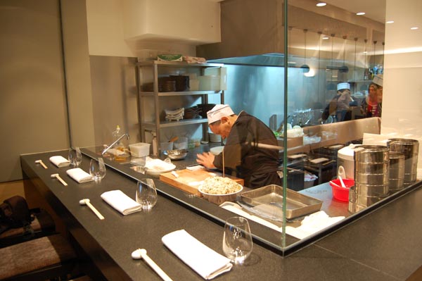 <b>TAOKAN</b> - 8, rue du Sabot - Paris VIe<br/><br/>Le mange-debout en granit noir et les vitres sont supportés par une tubulure inox<br/>L'éclairage technique, nécessairement bleuté, tranche visuellement avec la chaleur de la salle.